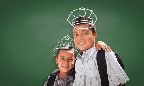 Young Hispanic Student Boy Wearing Backpack Front Of Blackboard with Fireman Helmet And Policeman