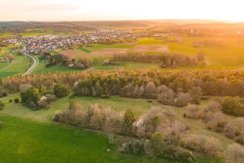 Panorama of a village with fields and wooded hills in golden evening light, e-bike tour, old sports