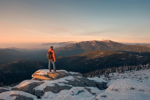 A hiker in a red jacket stands on a snowy peak in Siete Picos, Guadarrama Mountains, gazing at the