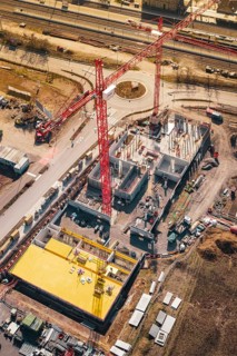 Compact construction site with high activity and red cranes, near a road and rails, new Mühlacker