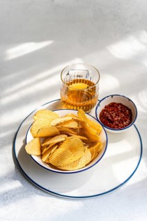 Crispy homemade chips served alongside a spicy dip and a refreshing drink, perfect for snacking. A