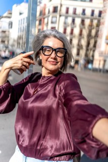 Mature woman happily capturing a moment by herself, holding a cup of coffee and wearing glasses,