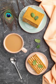 Homemade honey cake with milk cream and mint with cup of coffee on a black concrete background and