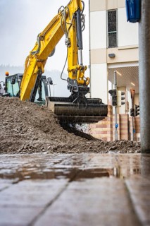 Large excavator moving earth on a construction site in the rain, building in the background,