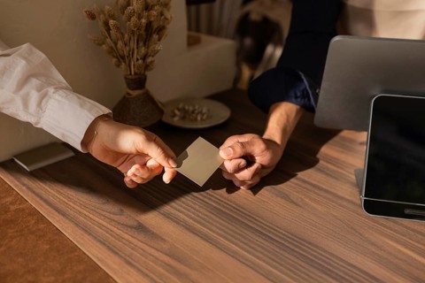 A customer and salesperson exchange a card over a stylish wooden counter in a cozy bag store, with