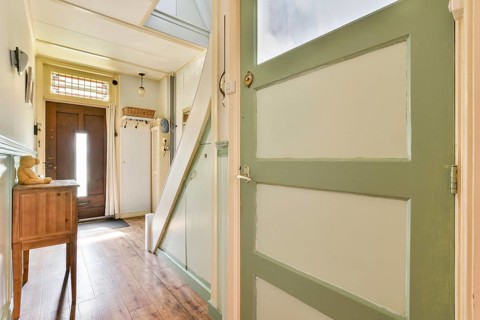 A bright and inviting indoor hallway featuring light-green walls and a wooden floor. The space is
