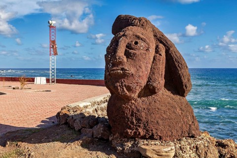 Moai statue stands against a backdrop of the ocean under clear skies and clouds, The Moai Statues