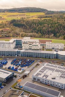 Large modern building with solar systems in a rural area next to a forest, shortly in front of