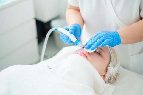 A professional cosmetologist uses an electronic device to apply blue light treatment during a