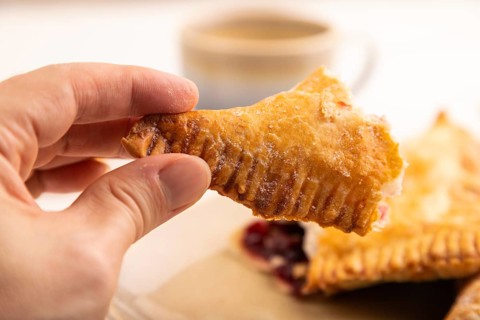 Triangles Pie, Puff Pastry, Samsa with cherry jam with hand on white wooden background, cup of