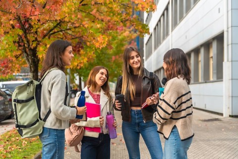 Young female students and friends engaging in conversation while walking on a university campus