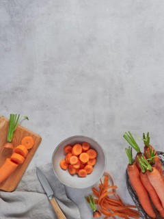 Top view of gray cement kitchen countertop with raw, whole and sliced carrots with copy space