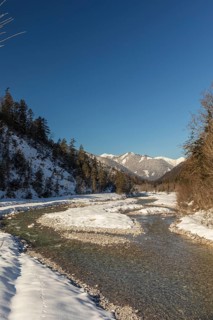 The Riss creek flowing through a snow covered landscape in the Eng valley. Sunny day with blue sky