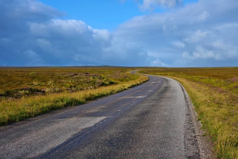 A long, empty road runs through a vast grassland under a dramatic sky, Tongue, Lairg, Scotland,