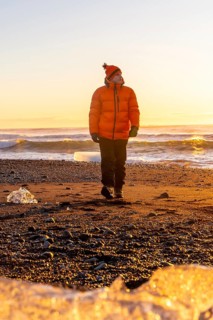 A tourist in an orange jacket walking at sunrise on Diamond Beach Iceland in winter
