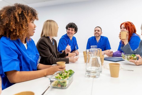 Diverse group of medical staff in scrubs and business attire enjoying a meal and conversation