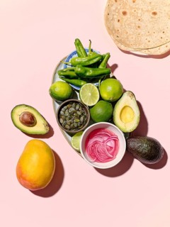 Top view of vibrant taco components spread on a pink background, featuring green peppers, limes,