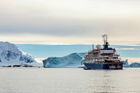 A ship sails through a tranquil Arctic landscape, past majestic icebergs under a cloudy sky, cruise