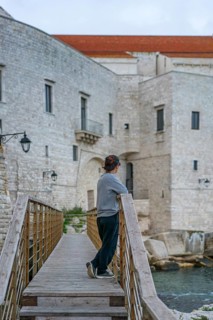 A visitor leans on a wooden bridge, gazing at the historic stone castle of Polignano a Mare, a