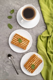 Homemade honey cake with milk cream and mint with cup of coffee on a gray concrete background and