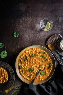 Flat lay composition of hearty vegan chickpea curry soup bowl and glass of lime water on black