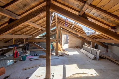 Sunlit attic with wooden beams and scattered construction materials showcases a renovation in
