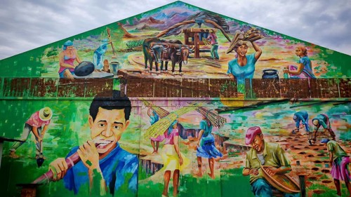 Mural, graffiti depicting scenes of agricultural life with people at work, hangar, warehouse at the