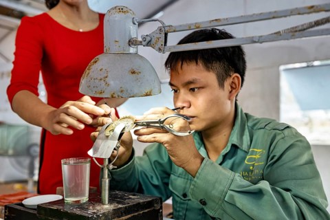 Man working concentrated with tools, assisted by a woman, pearl farm in Halong Bay in Vietnam