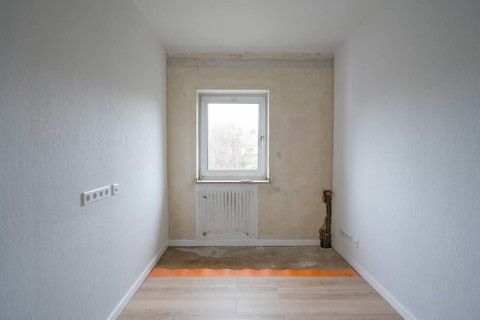 Empty room is being renovated, walls are partially wallpapered, laminate on the floor, heating