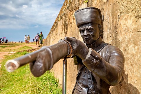 Bronze statue of a soldier pointing a rifle at a target, next to a wall, statue in the historic