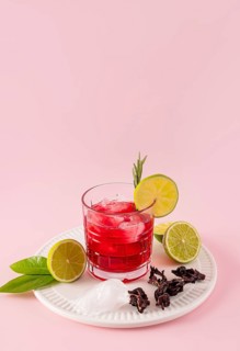 Vibrant hibiscus tea with ice and lime slices on a white plate. Enhanced with hibiscus flowers and