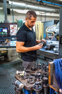 Vertical photo of a concentrated male caucasian technician working with milling machine in a cnc