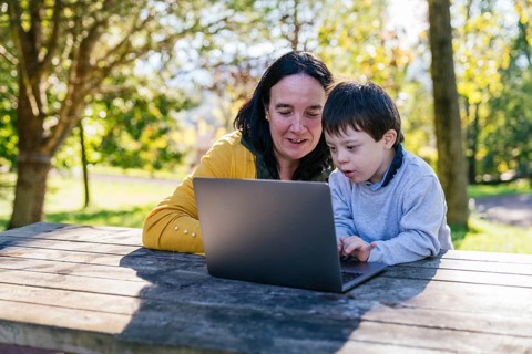 A mother and her son with Down syndrome engage in learning with a laptop while sitting at a wooden