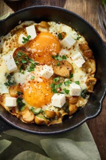 Fried eggs with spinach, mushrooms, grated cheese and feta cheese in small cast iron skillet. Top