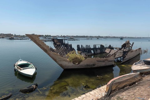 An abandoned burned out hull of a fishing boat with green plants growing inside it on the banks of