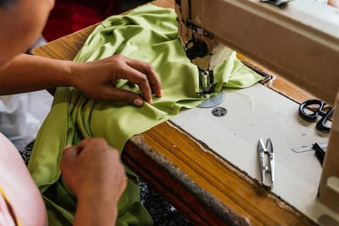 Close up of asian seamstress hands guiding green fabric through a sewing machine. Essential tools