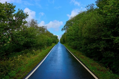 A straight road runs through a wooded landscape under a blue sky after rain, Tarbert, Loch Fyne,