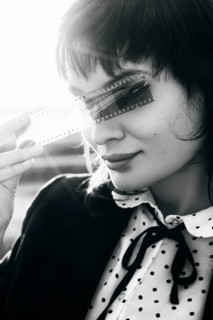 Black and white portrait of a woman holding a film strip over her eyes, evoking a sense of mystery