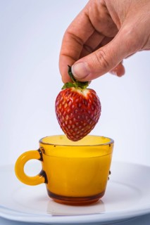 A pretty strawberry dipping into a cup of milk by a woman's hand