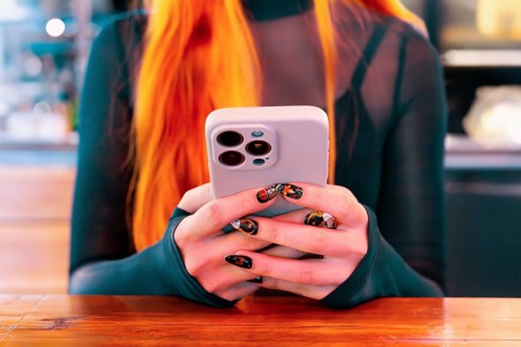 A woman with red hair and decorative nails holds a smartphone while exploring an Asian food market