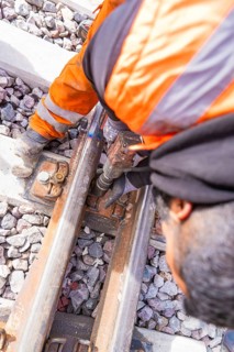 Construction workers in orange protective clothing work on the rails in a ballast bed, rail