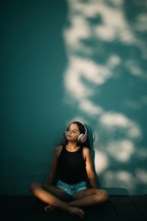 A serene teen girl with headphones sits cross-legged against a wall, immersed in music. Tree