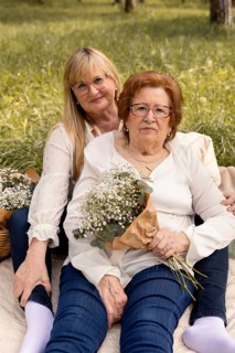 A mother and daughter share a tranquil moment outdoors, seated on a blanket amidst nature. They