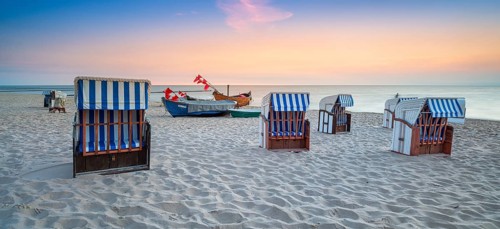 Beach chairs and fishing boats with red flags on fine sandy beach at sunrise, Baltic resort