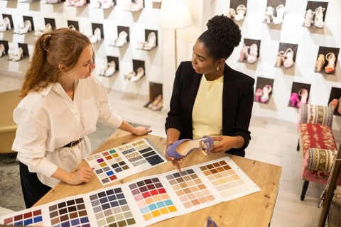 Two women collaborate over color swatches and shoe selection in a bridal studio environment,