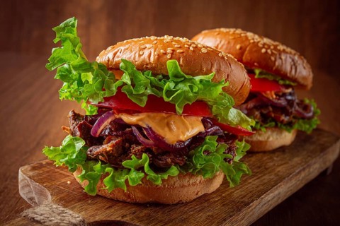 Two burgers are stacked high with fresh lettuce, tomato slices, grilled onions, and a savory sauce.