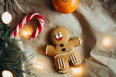 A cheerful gingerbread man cookie is surrounded by a candy cane, orange, and warm glowing lights