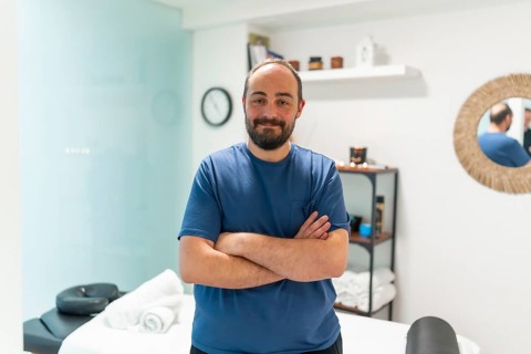 Male professional masseur standing with crossed arms in a bright wellness spa clinic, providing