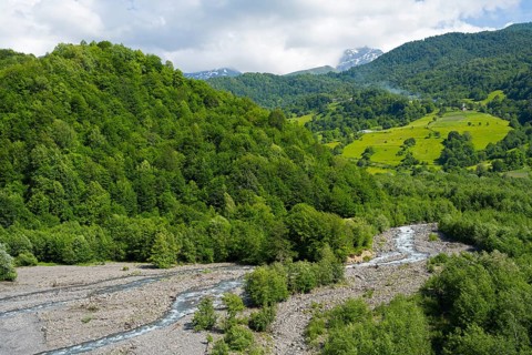 Picturesque landscape with a river running through forests and rolling mountains under cloudy sky,
