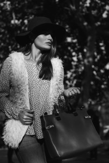 Black and white portrait of a fashionable woman outdoors wearing a hat, furry vest, and carrying a